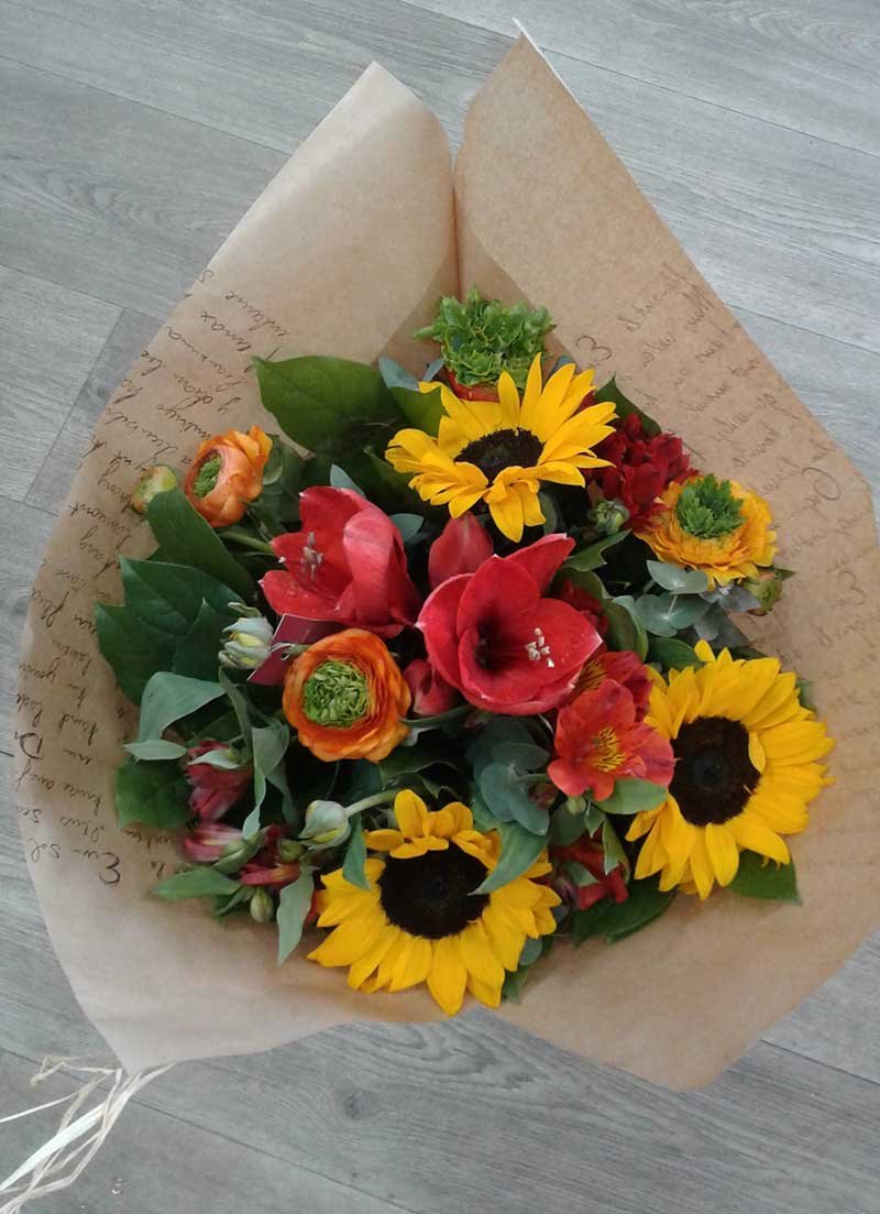 Bouquet champêtre de tournesols, amaryllis et renoncules dans un emballage kraft