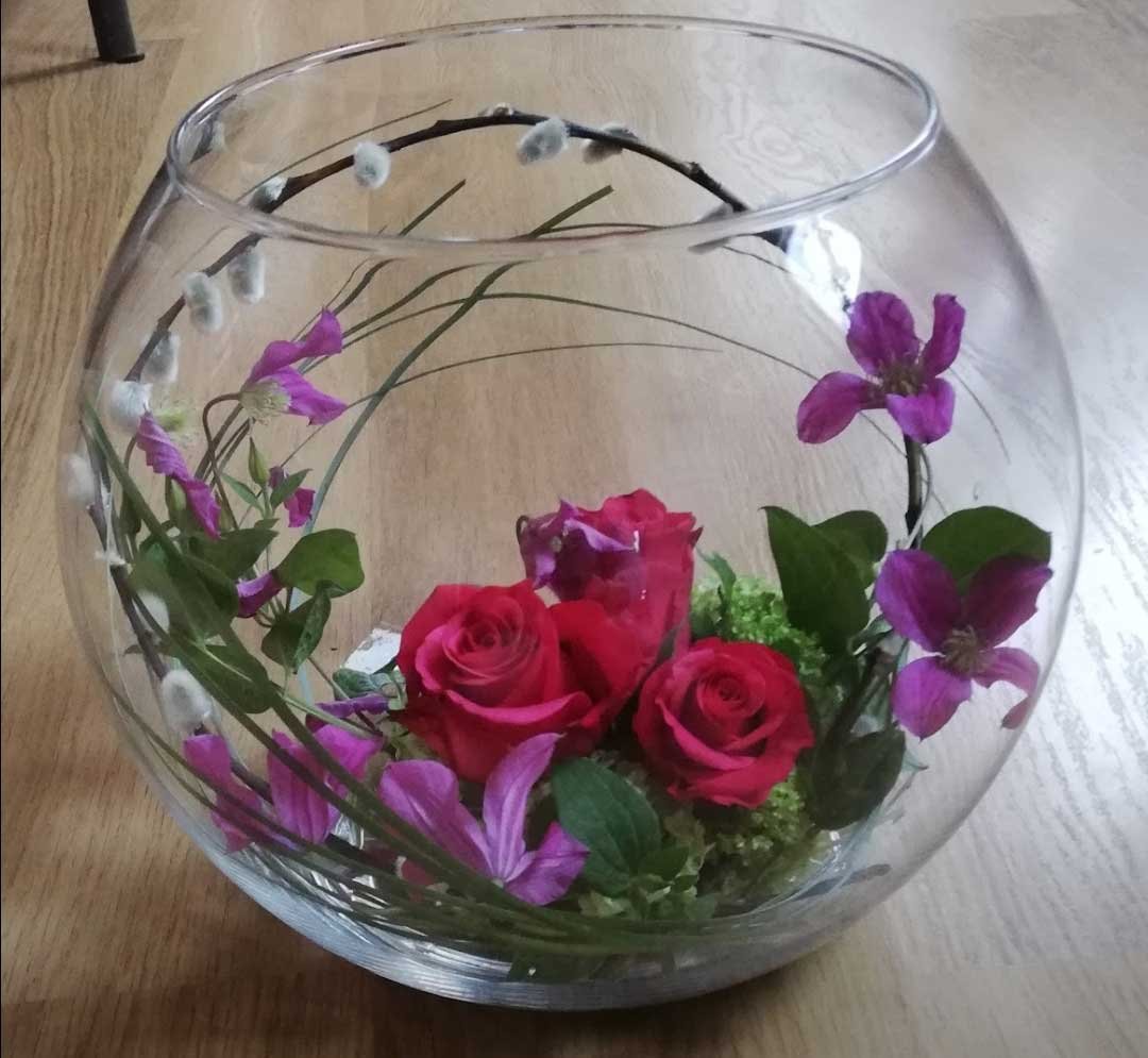 Composition dans une bulle de verre : roses rouges, clématites et chatons de saule